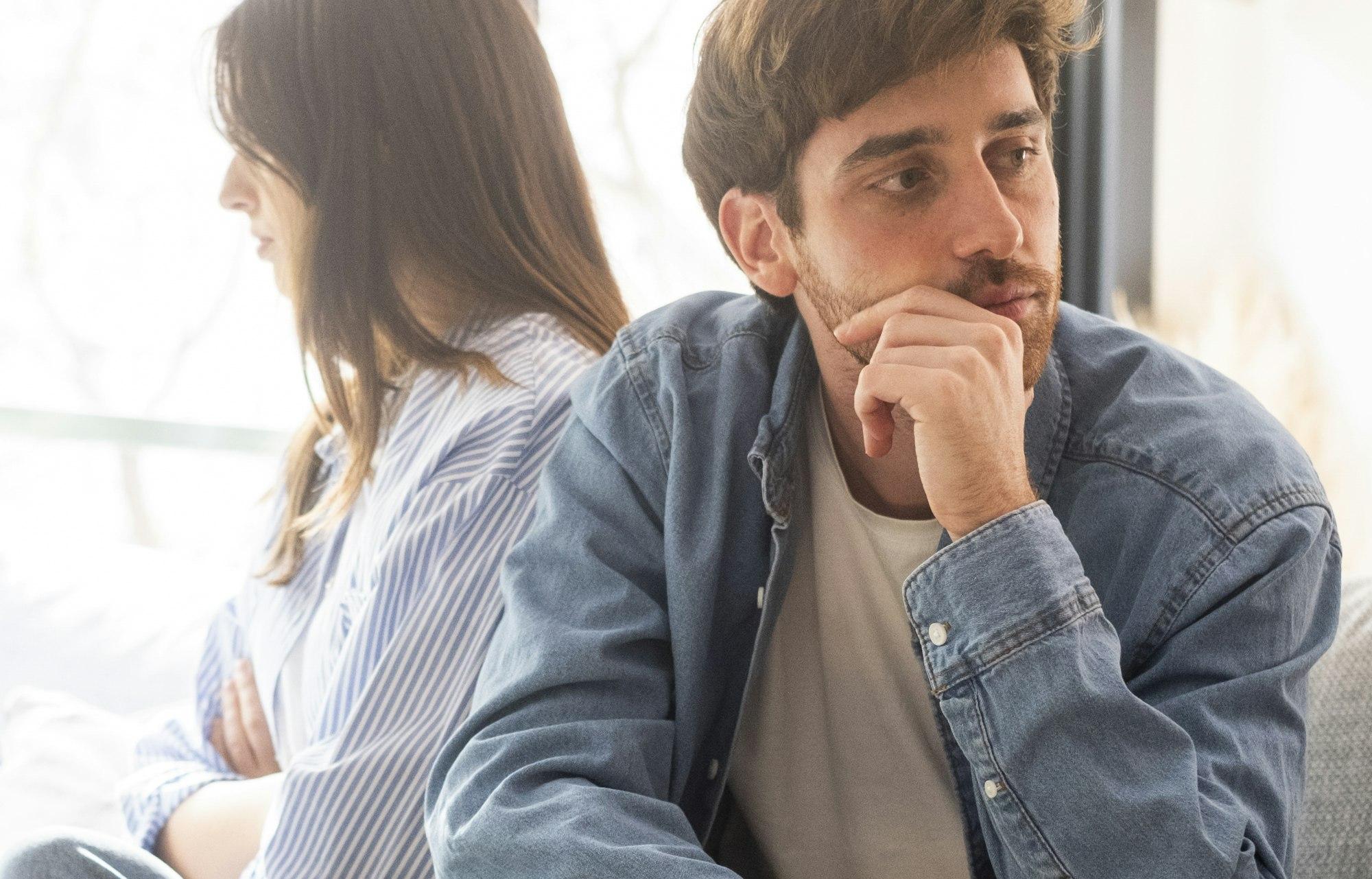 Engaged couple with relationship problems sitting on the sofa with their backs to each other