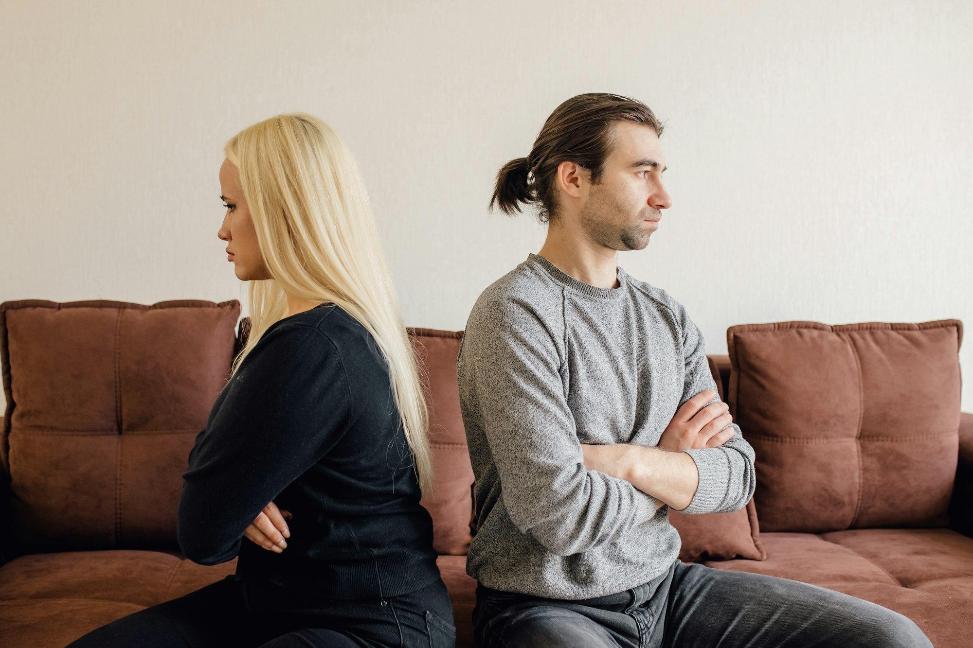 Focus on stressed angry young couple sitting separate on couch.