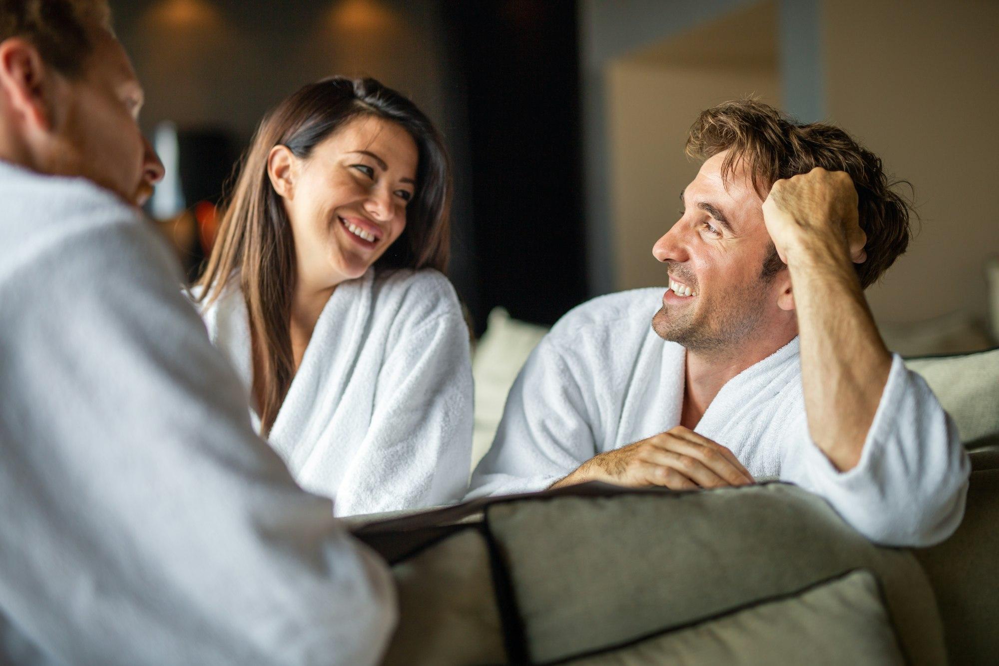 Group of happy people enjoying wellness relax weekend. Woman with two handsome men in bedroom.