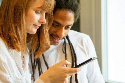 Interracial couple prepare a salad together with the help of their cell phone.