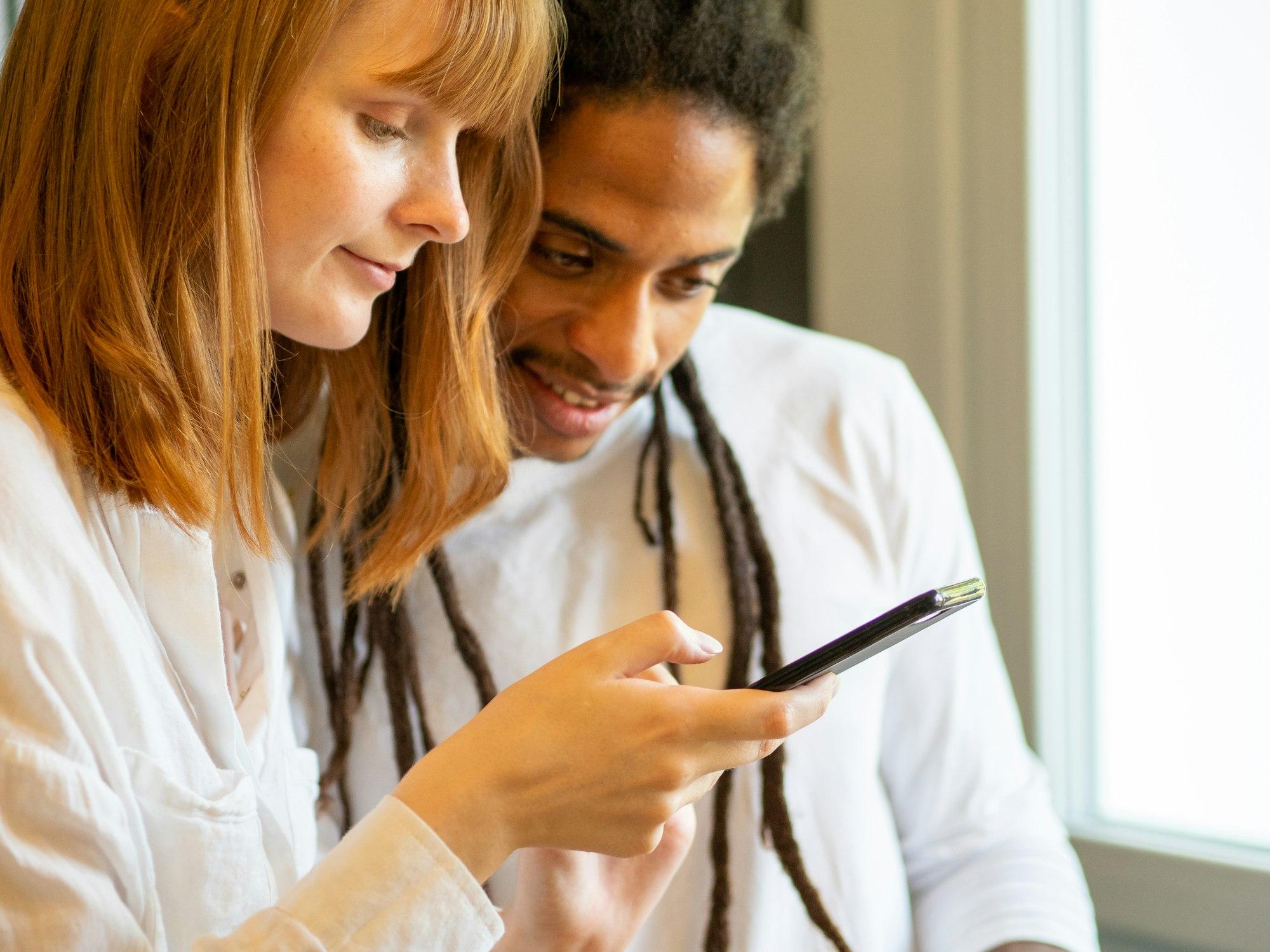 Interracial couple prepare a salad together with the help of their cell phone.