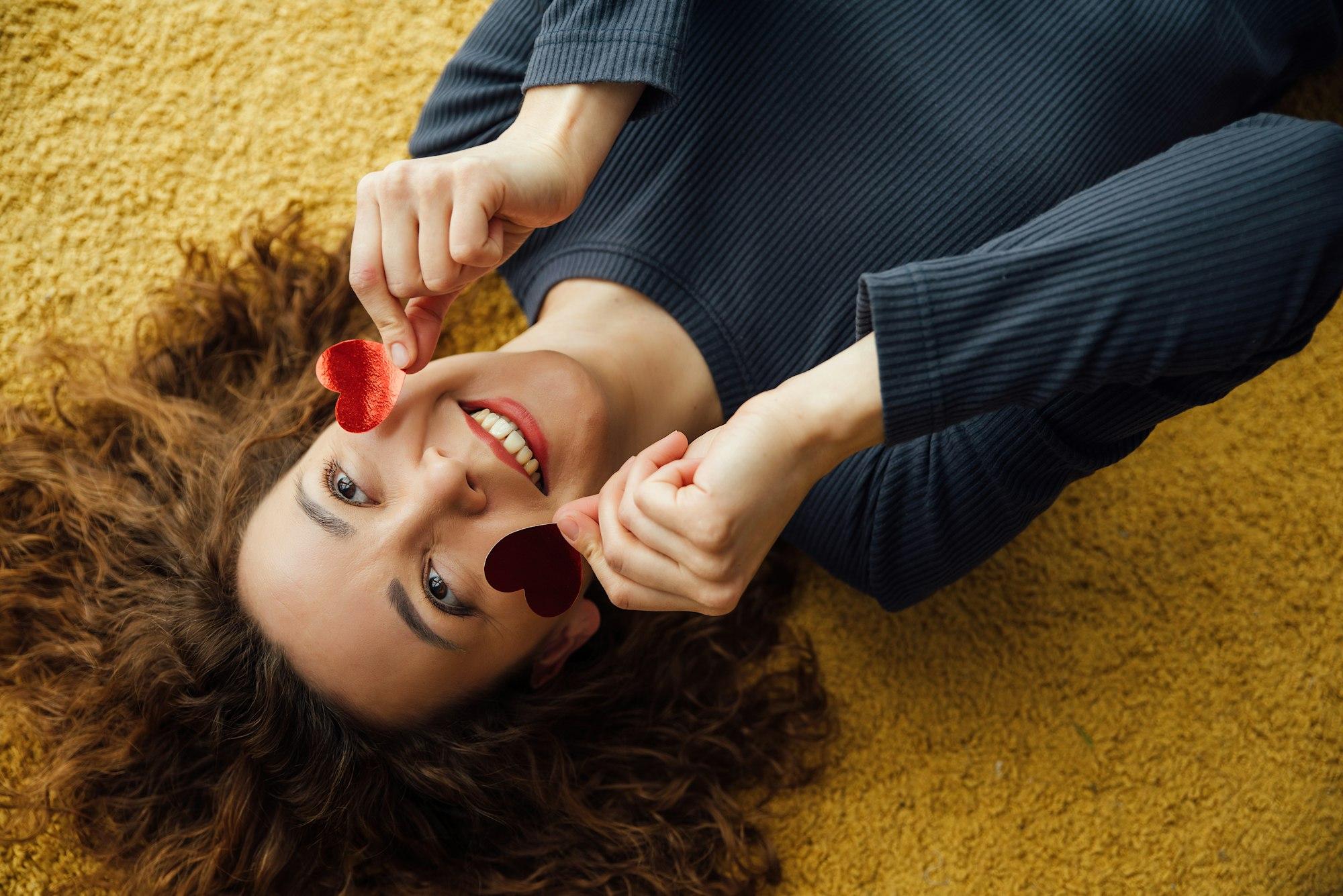 Smiling woman in love, coquettishly holding hearts near her face