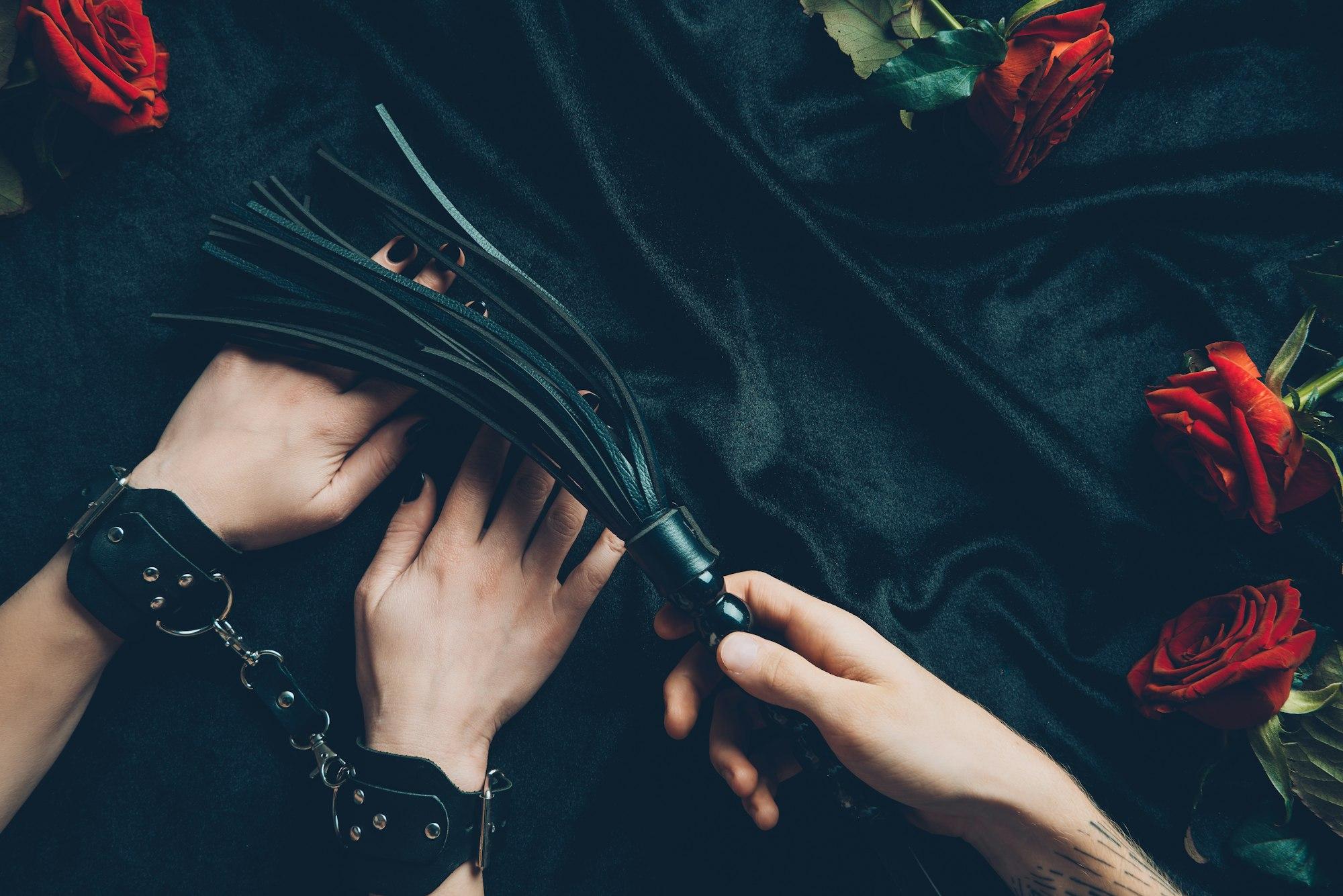 cropped shot of man holding black whip and woman in leather handcuffs