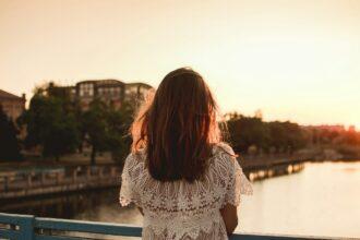 Back view backlight portrait of single woman on the bridge over the river on sunset city warm light