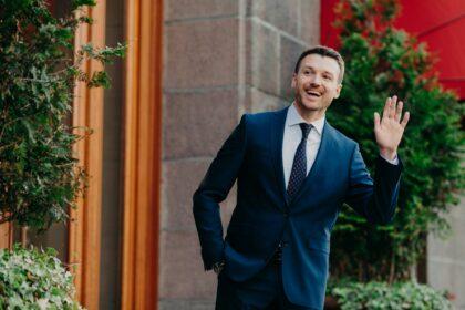 Businessman in formal clothes waves with hands as sees colleague into distance.