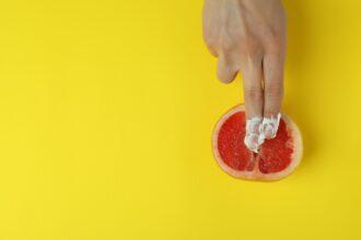 Female hand with whipped cream and grapefruit on yellow background