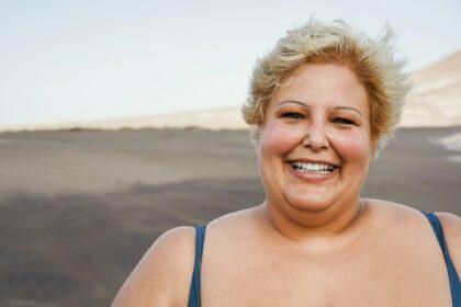 Portrait of curvy woman smiling on camera wearing bikini at the beach - Focus on face