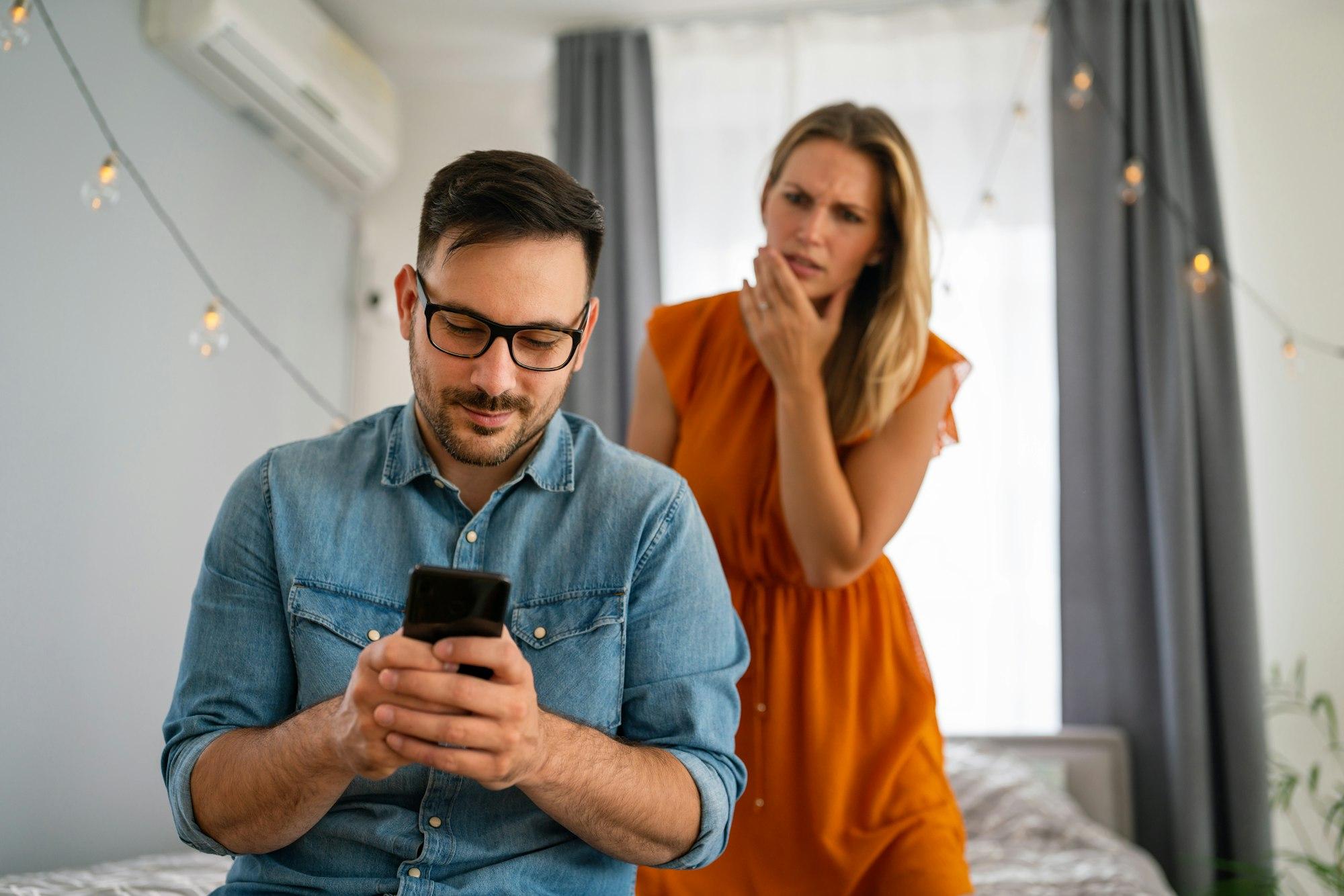 Jealous woman spying boyfriend and watching his mobile phone. Couple cheating jealousy concept