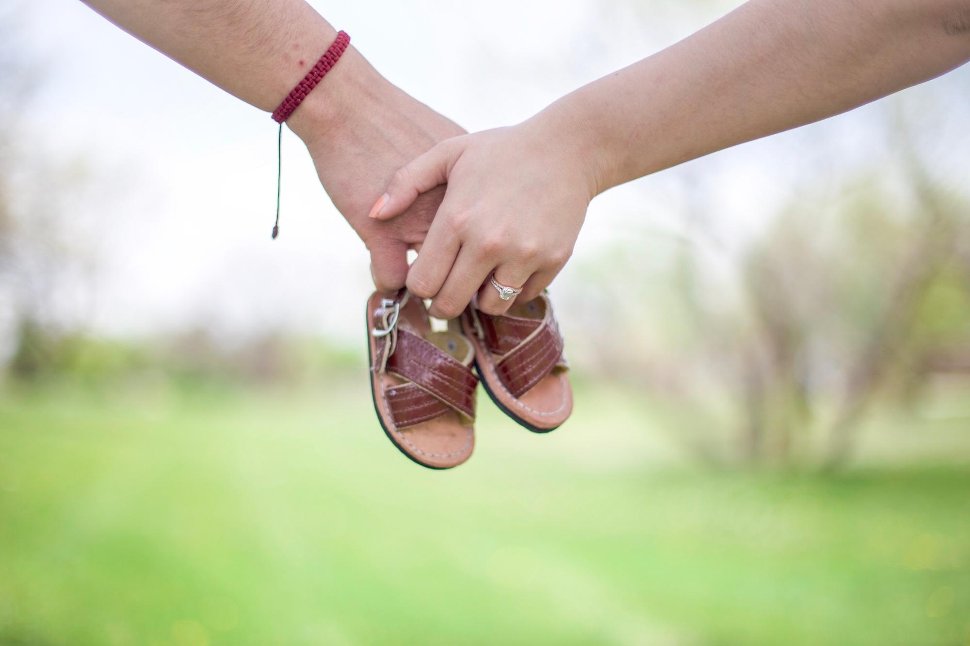 Couple holding hands and holding baby shoes to announce their pregnancy