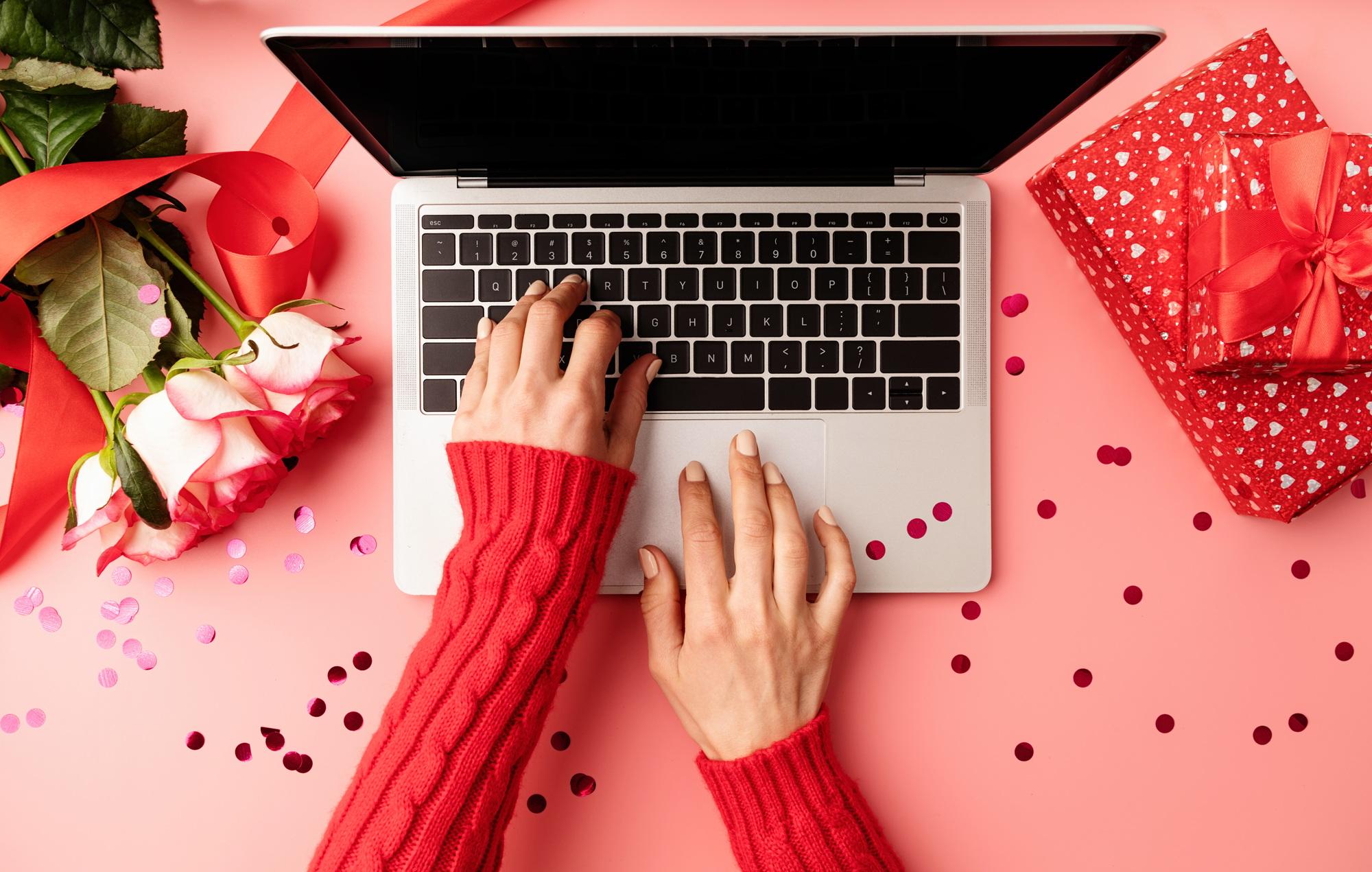 Valentines Day concept. Female hands typing on the keyboard, top view on pink background. Top view o