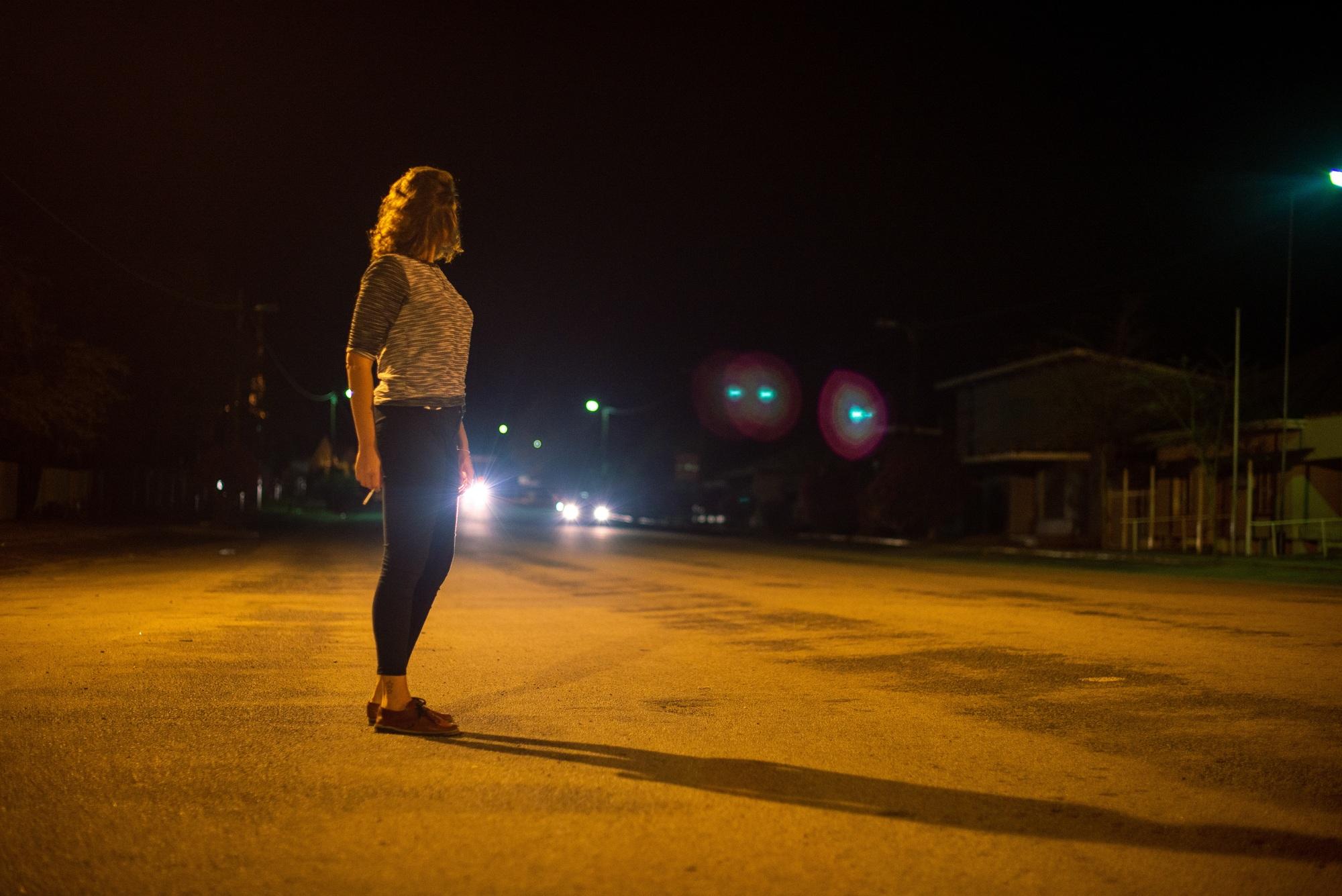 Young woman working the street waiting for a client with vehicles approaching in background