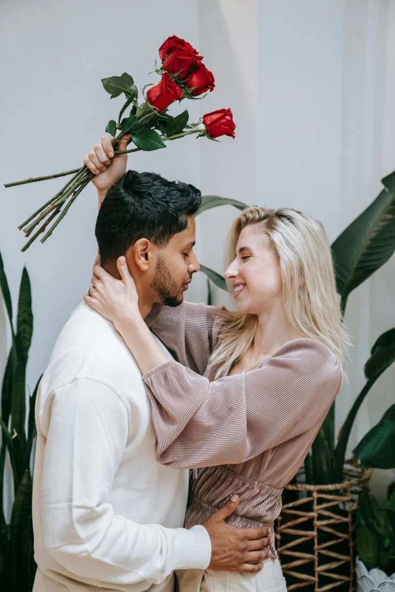 Affectionate couple embracing indoors with a bouquet of red roses, symbolizing love.