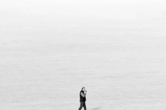 Black and white image of a lone walker in an expansive field, emphasizing solitude and minimalism.